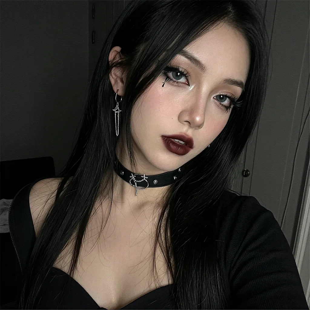Black-haired woman with green-blue eyes and dark lipstick wearing studded leather choker and star earrings