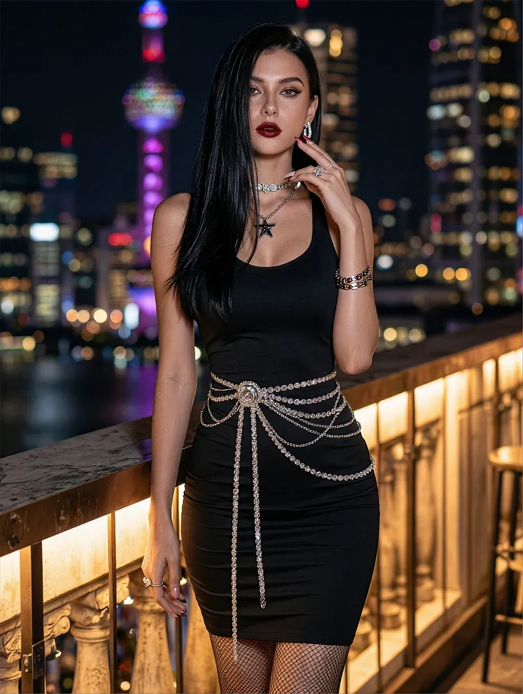 Black-haired woman in black tank dress with crystal chain belt on rooftop balcony with city skyline at night